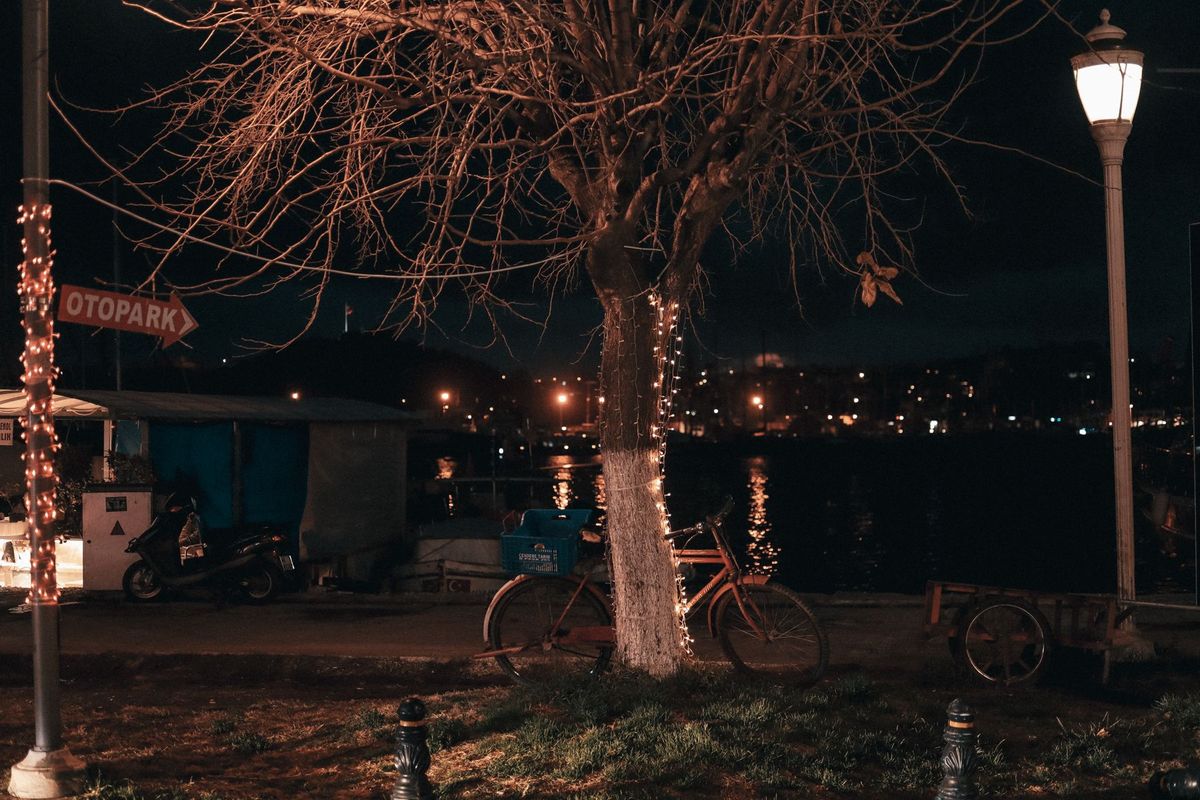 A serene urban night scene with a bicycle by a river, city lights reflecting on the water