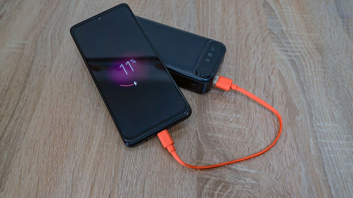 A smartphone charging from a power bank with an orange cable on a wooden table
