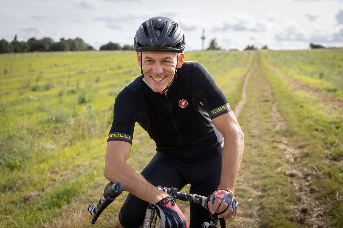A smiling male cyclist wearing a helmet and sportswear on a countryside path