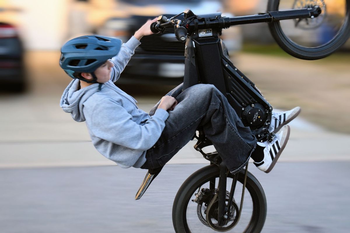 A teenager performs a wheelie on an electric unicycle outdoors