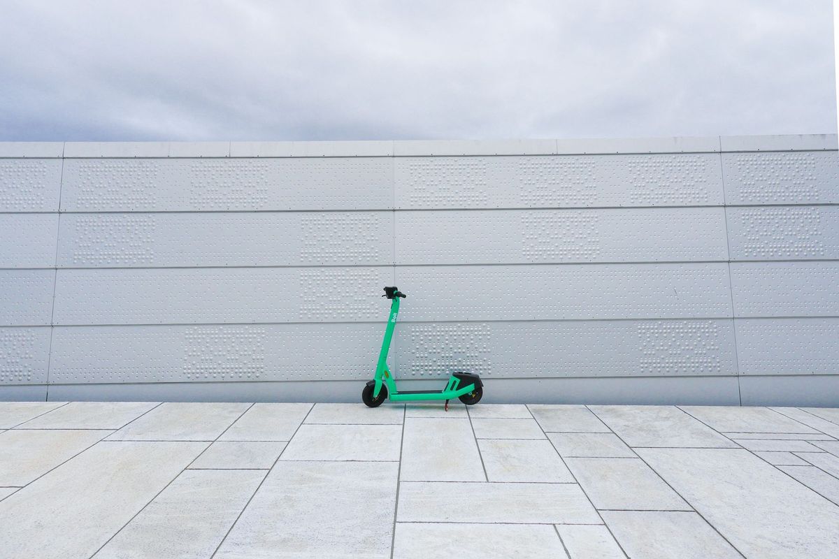 A vibrant green scooter parked against a textured white wall under a cloudy sky