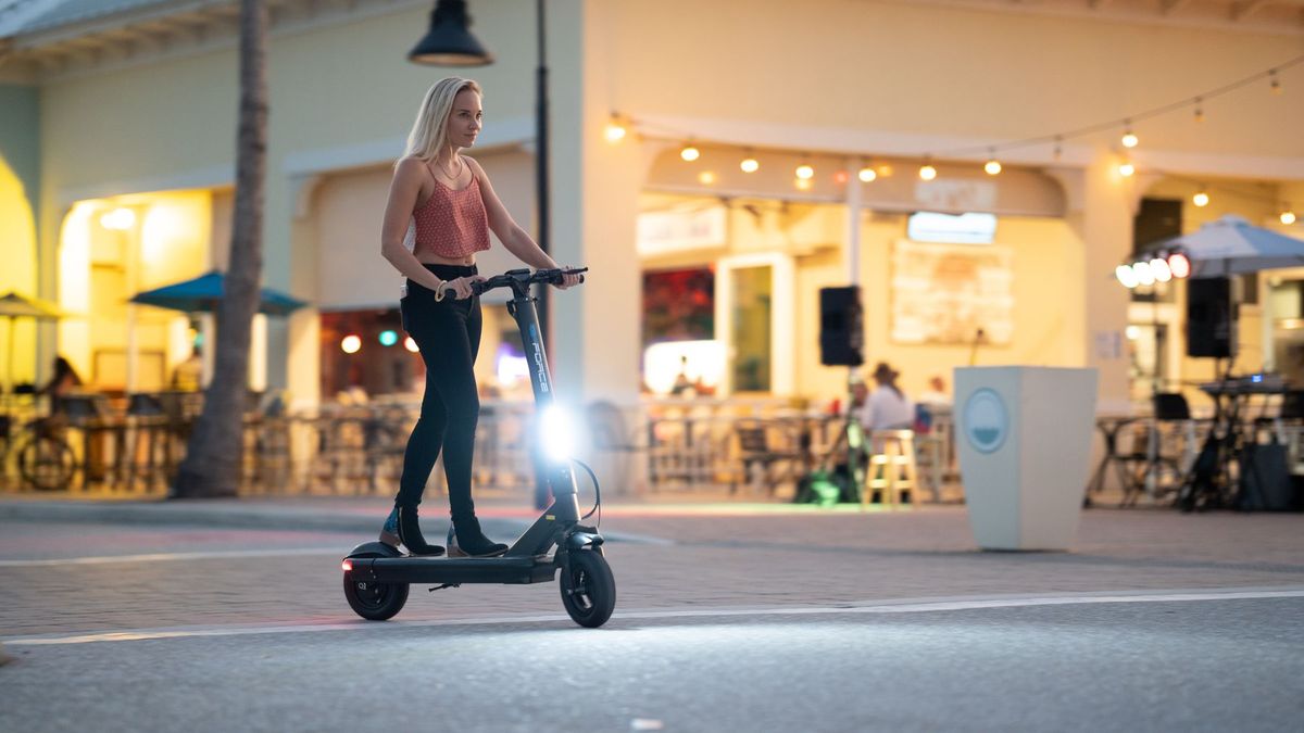 A woman rides an electric scooter on an illuminated urban street in the evening