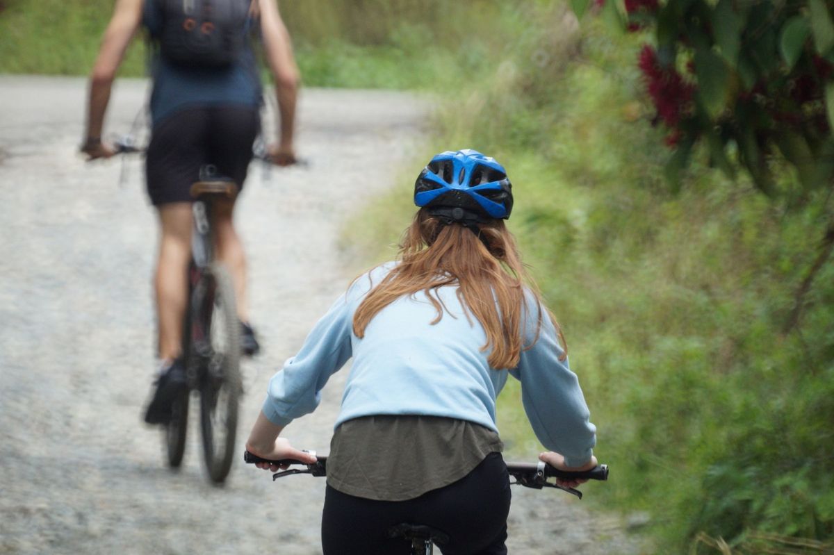 A woman with a helmet rides a bike on a rural path with another cyclist ahead