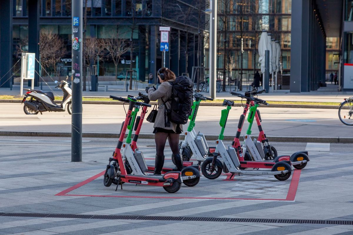 A young adult uses rental scooters at an urban parking spot