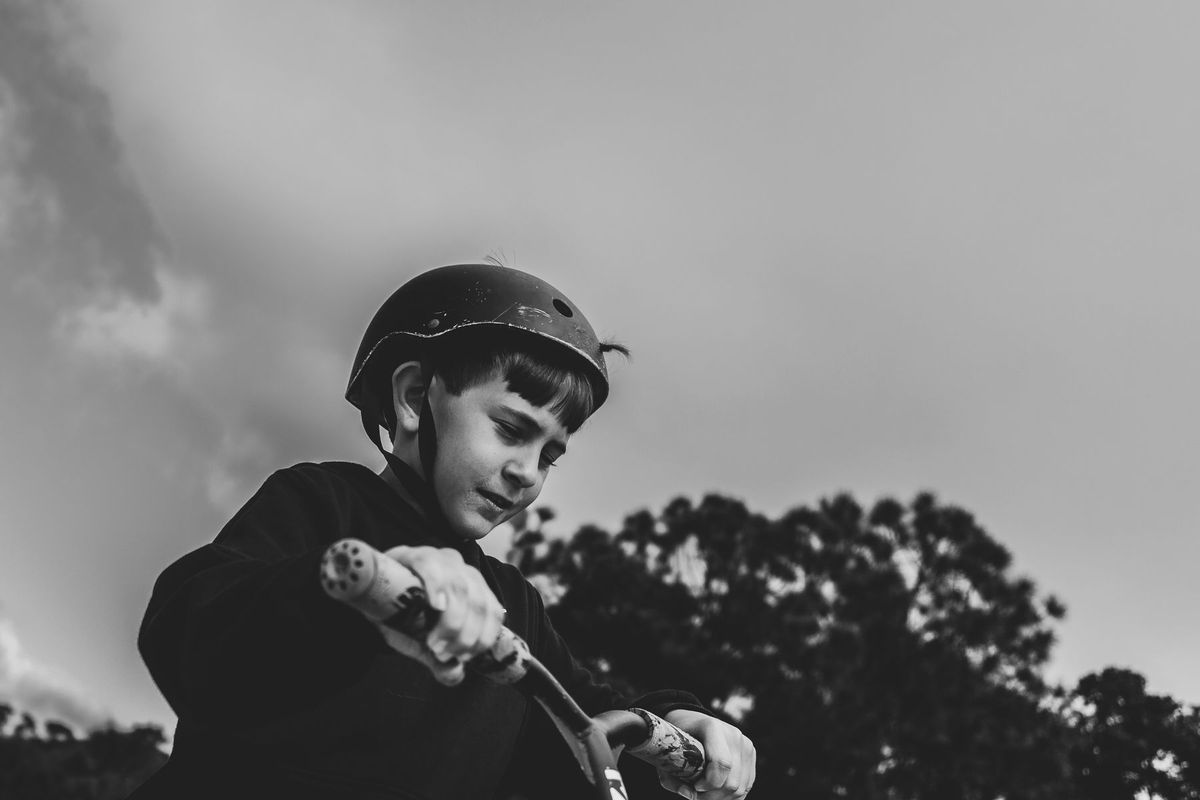 A young boy wearing a helmet riding a scooter outdoors in a black-and-white photograph