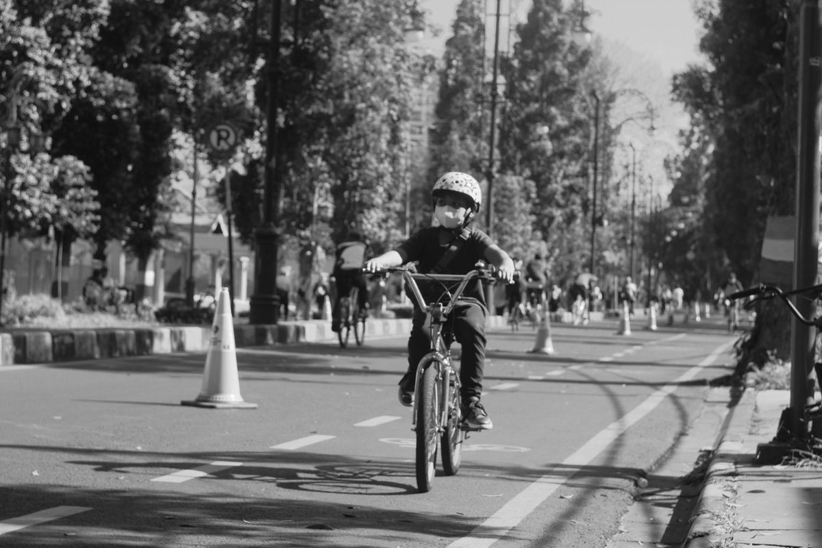 A young child rides a bike down a tree-lined street
