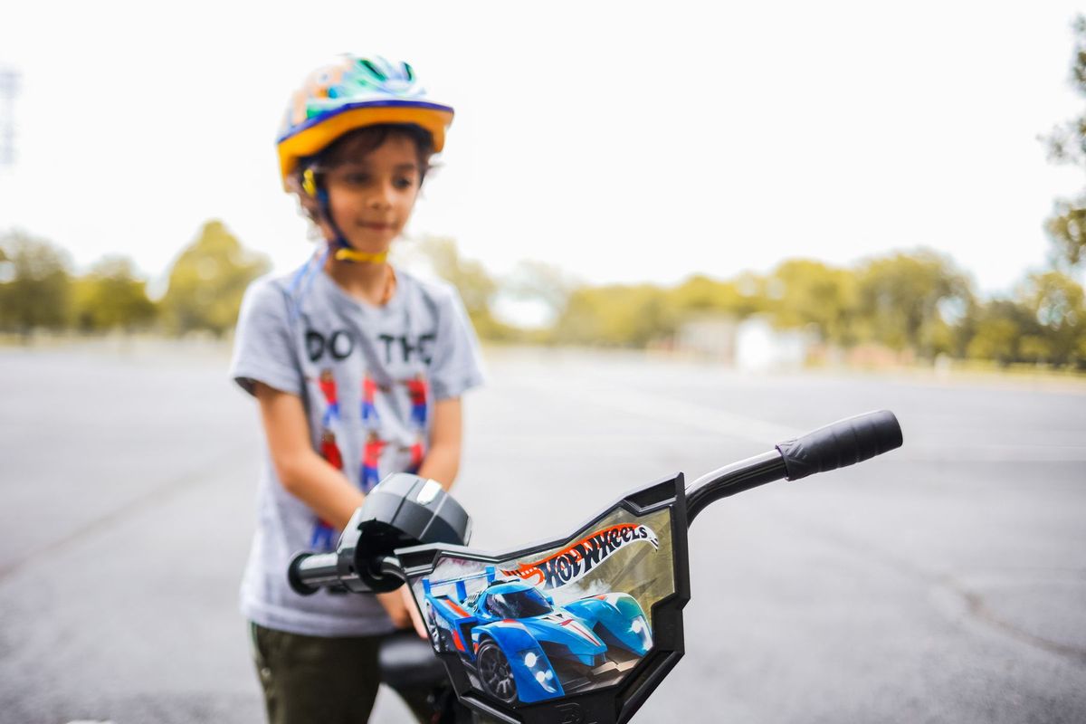 A young child wearing a helmet stands next to a bicycle in a park setting. Perfect for themes of childhood activity and safet