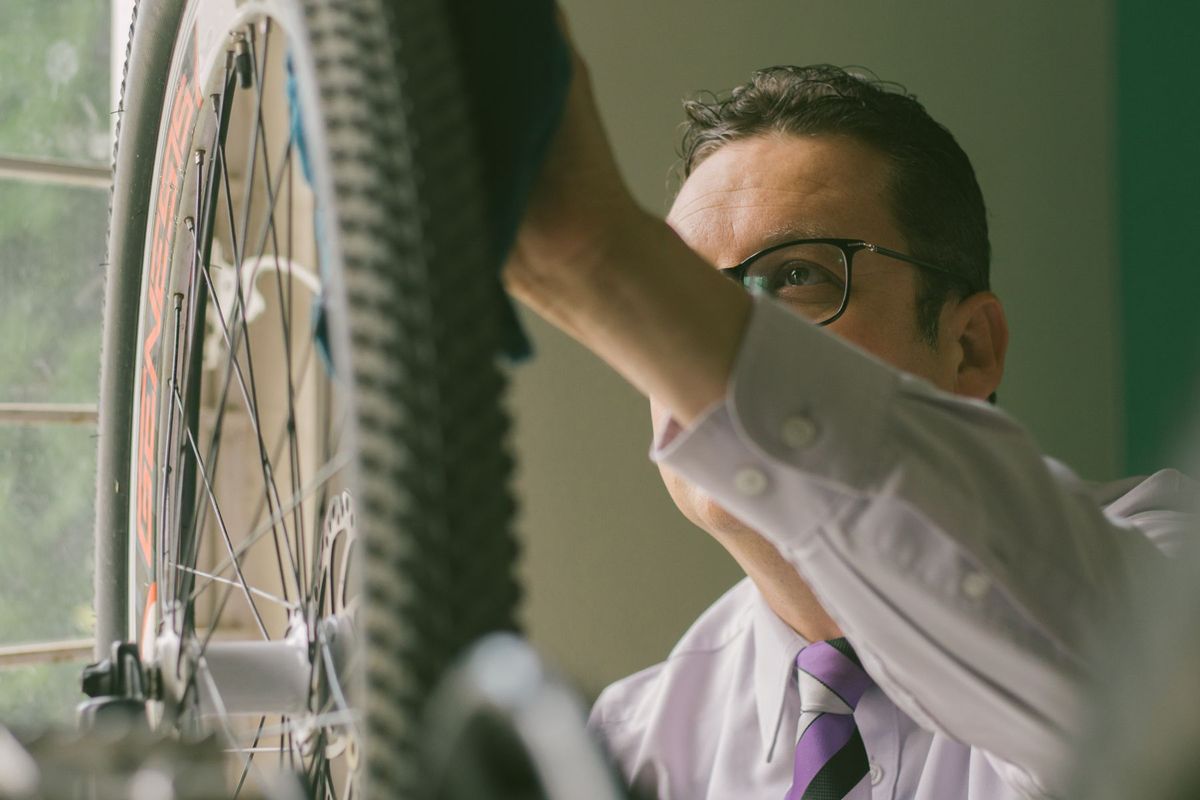 Adult man in a white shirt repairing a bicycle wheel indoors, using a cloth
