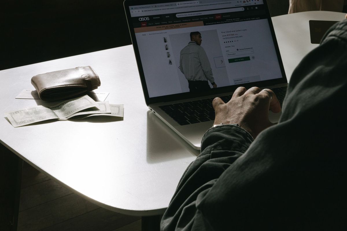 Adult man shopping for clothes online at home using a laptop, with a wallet on the table