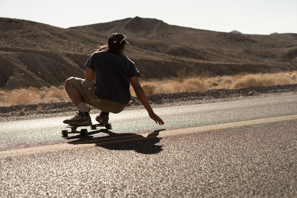 An exciting image of a longboarder riding on a desert road