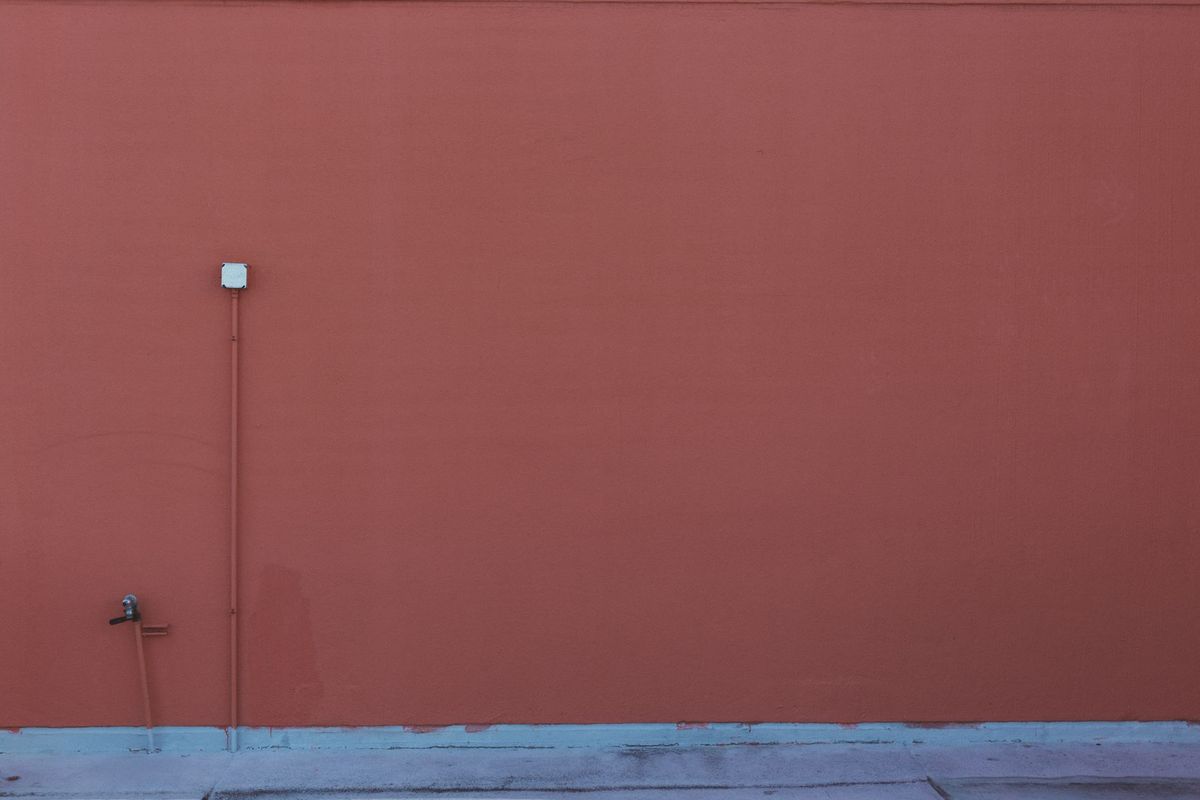 An orange-painted wall featuring a pipe and electrical outlet