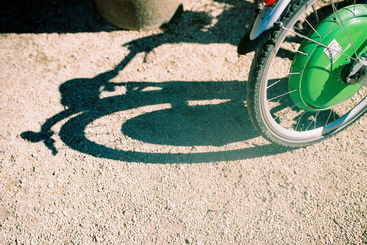 Artistic shadow of a bicycle wheel captured on a gravel path in daylight