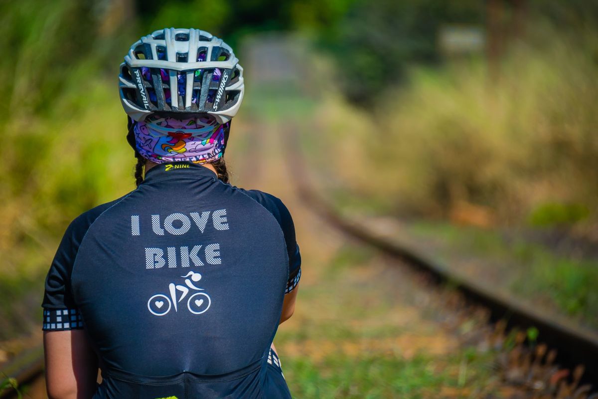 Back view of a cyclist wearing a jersey and helmet on railroad tracks in a natural setting