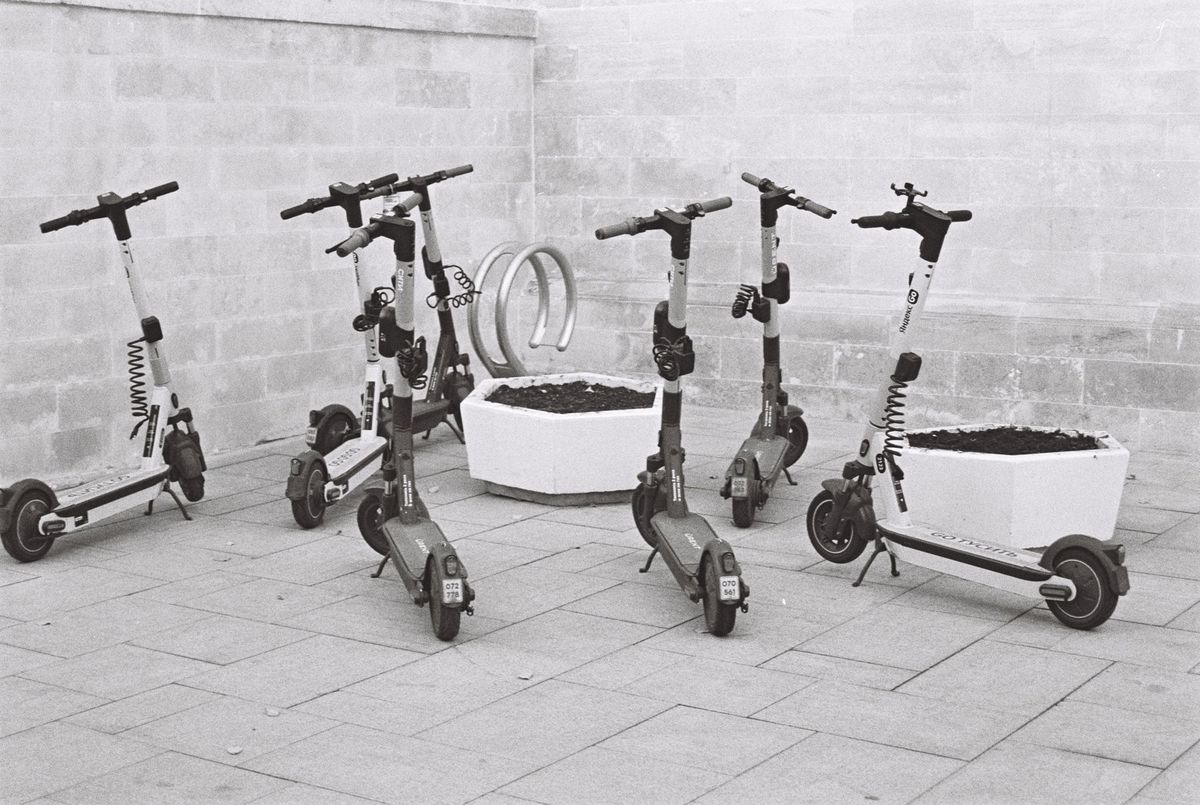 Black and white photo of several electric scooters parked beside concrete planters
