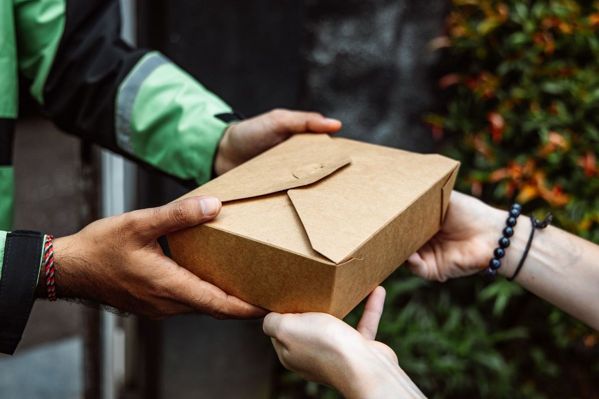 Close-up of a delivery person handing over a box to a customer outdoors