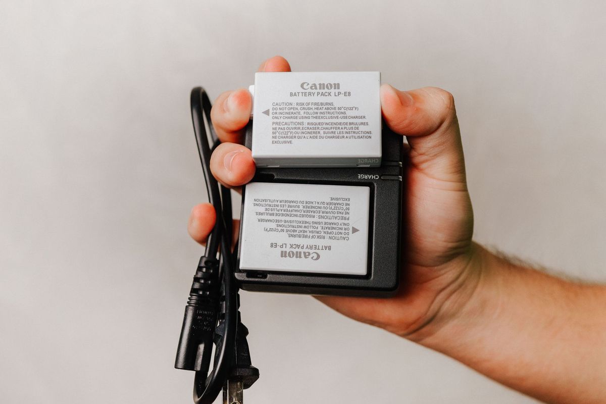 Close-up of a hand holding a Canon battery charger with cables, essential for photography electronics