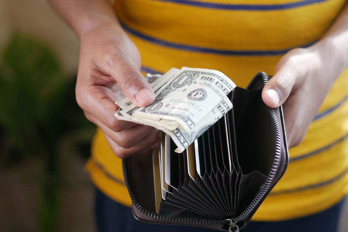Close-up of a person's hands holding US dollar bills and a wallet