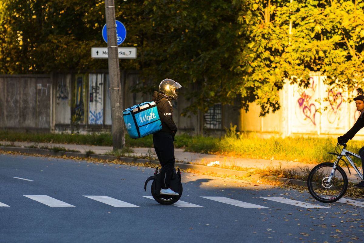 Delivery rider on electric unicycle crossing Riga street in evening light