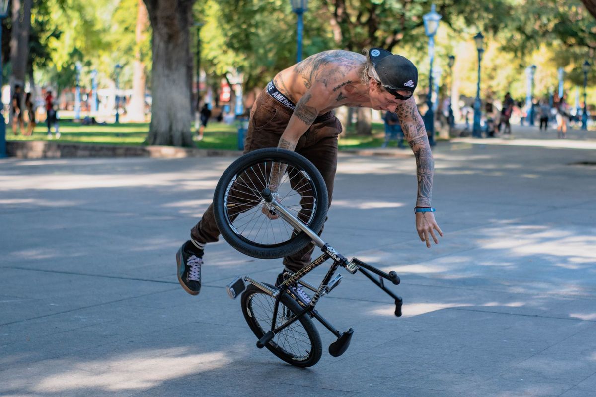 Dynamic shot of a shirtless BMX rider performing a trick in a bustling park
