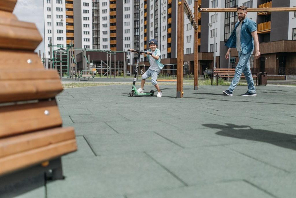 Father and son spending quality time at an outdoor playground, riding a scooter together
