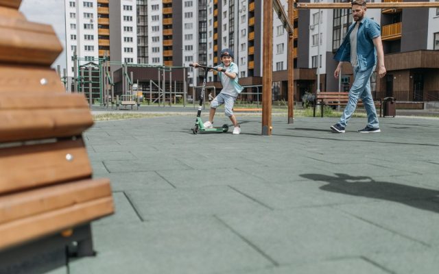 Father and son spending quality time at an outdoor playground, riding a scooter together