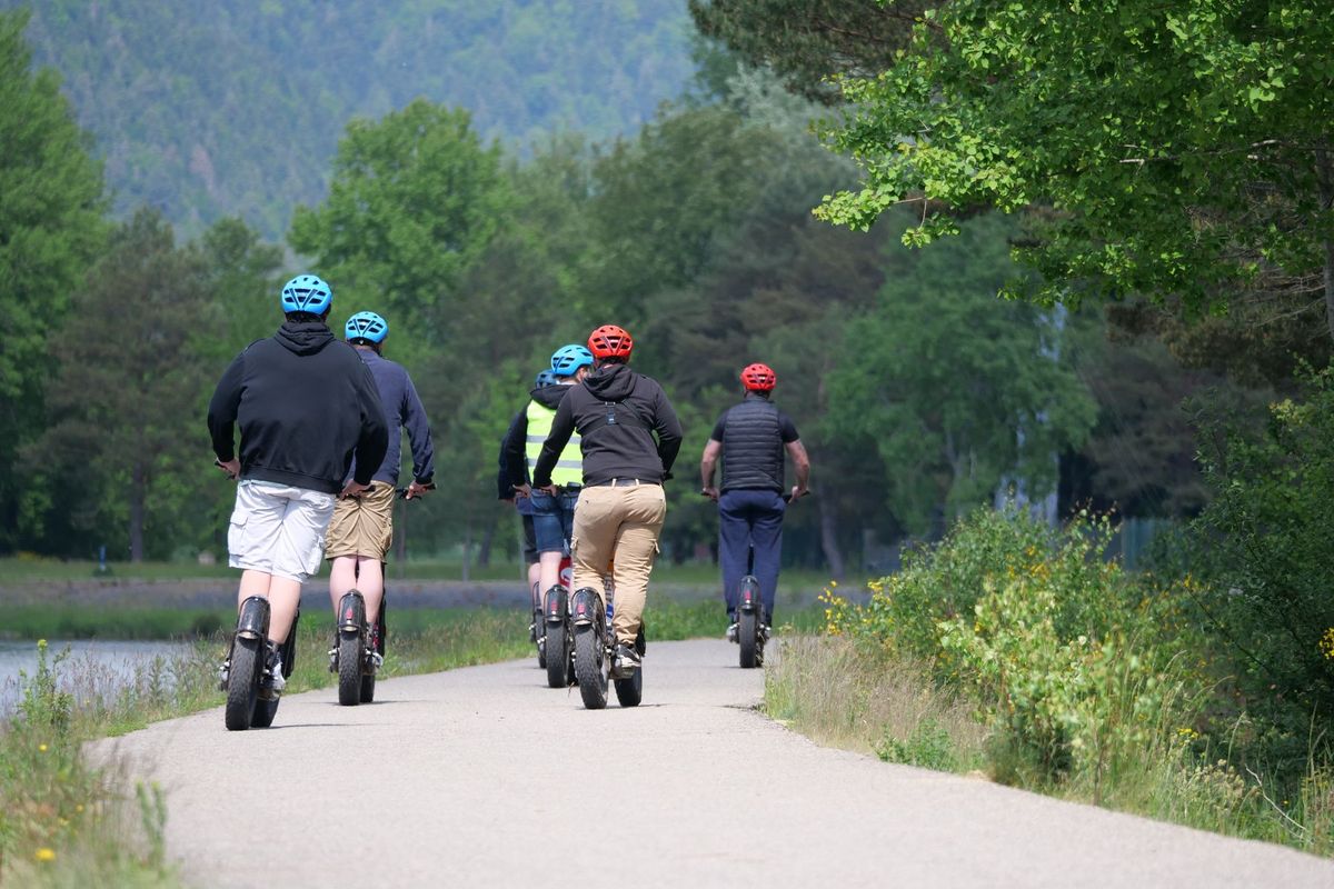 Five adults leisurely riding electric unicycles on a scenic outdoor path wearing helmets
