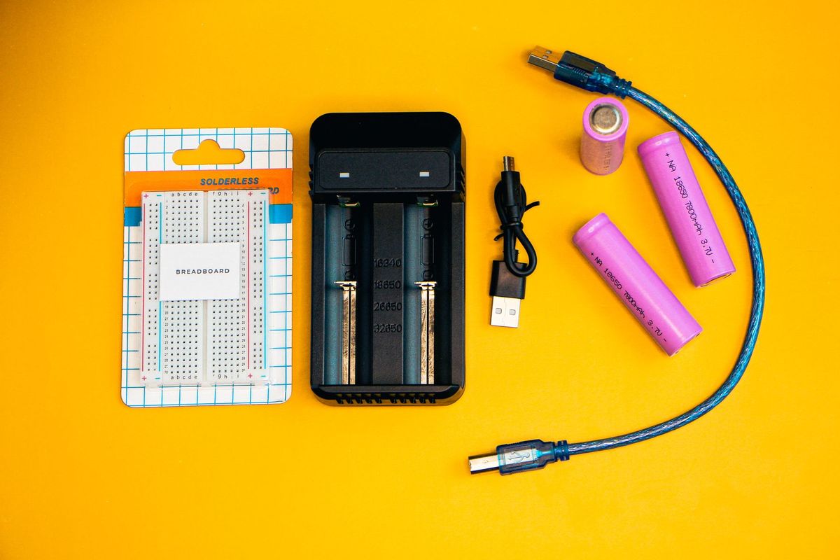 Flat lay of electronics including a breadboard and battery charger against a vibrant yellow backdrop