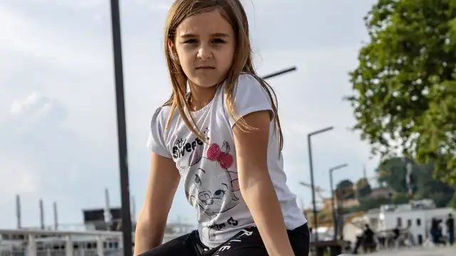 A girl kneeling beside a hoverboard on a waterfront path
