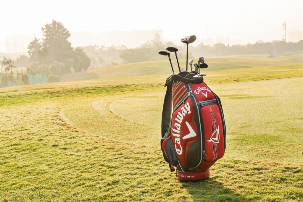 Golf bag and clubs on a sunny golf course with green grass