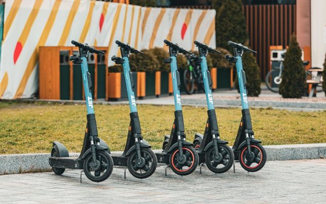 Group of five electric scooters neatly lined up outdoors, ready for rental use