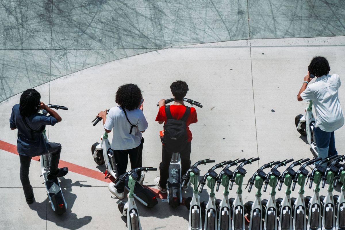 Group of young adults using electric scooters on a sunlit urban pavement