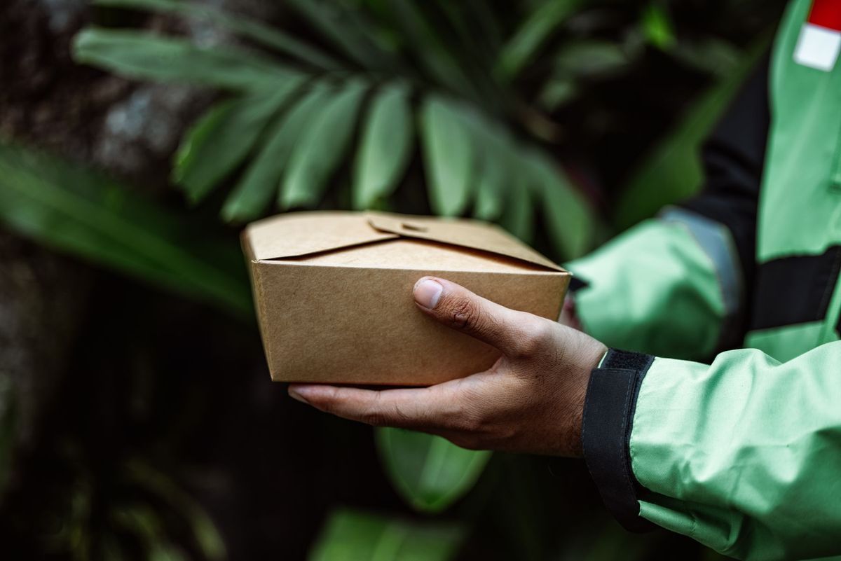 Hands holding an eco-friendly cardboard food box outdoors. Sustainable delivery concept