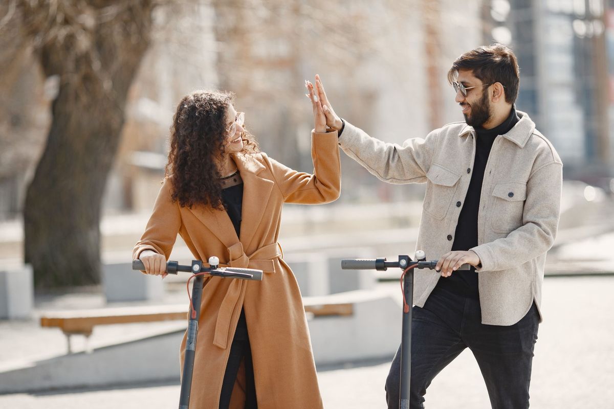 Happy couple sharing a high-five while enjoying a ride on electric scooters in an urban setting