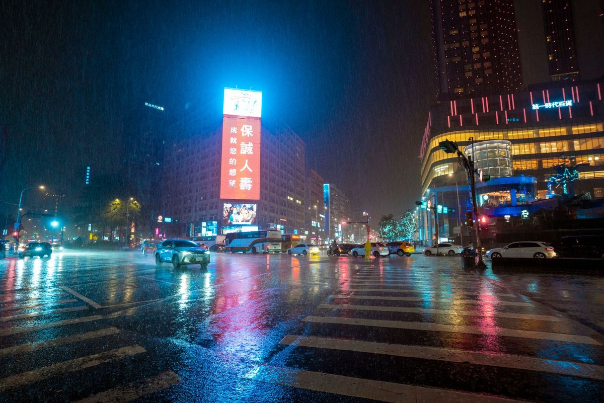 Illuminated city street at night with neon lights reflecting on wet pavement in rainy weather