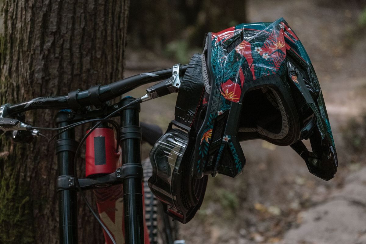 Mountain bike parked by a tree with a colorful helmet hanging from the handlebars
