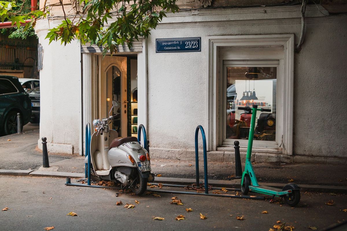 Parked scooter and electric scooter on Galaktioni Street, Tbilisi, with autumn leaves