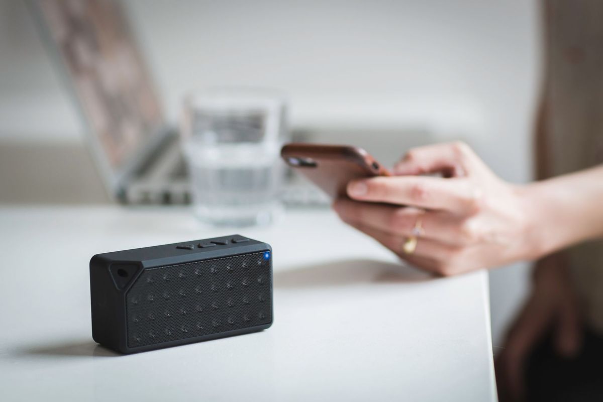 Person connecting a smartphone to a wireless speaker indoors, foreground focus