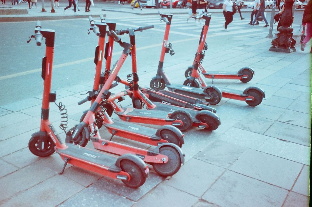 Red electric scooters lined up on an urban sidewalk with pedestrians in the background