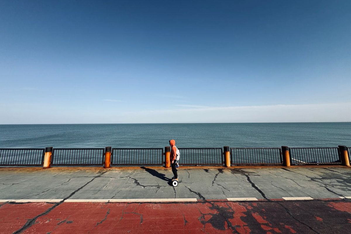 Rider on a hoverboard along an ocean promenade under a clear blue sky