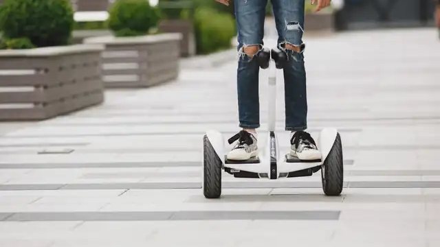 A rider on a Segway-style self-balancing scooter with a knee bar