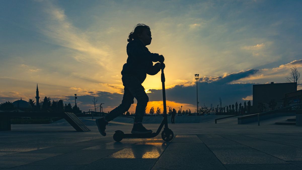 Silhouette of a child riding a scooter in an urban park at sunset