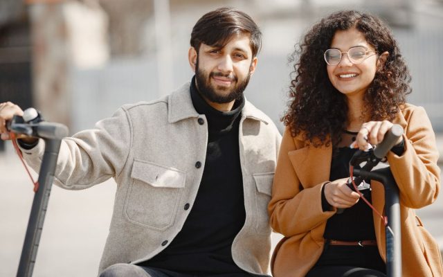 Smiling couple enjoying a ride on electric scooters outdoors in a sunny setting