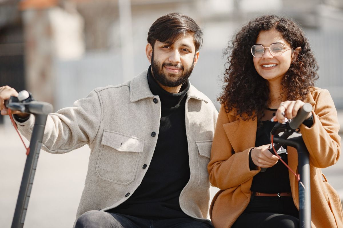 Smiling couple enjoying a ride on electric scooters outdoors in a sunny setting