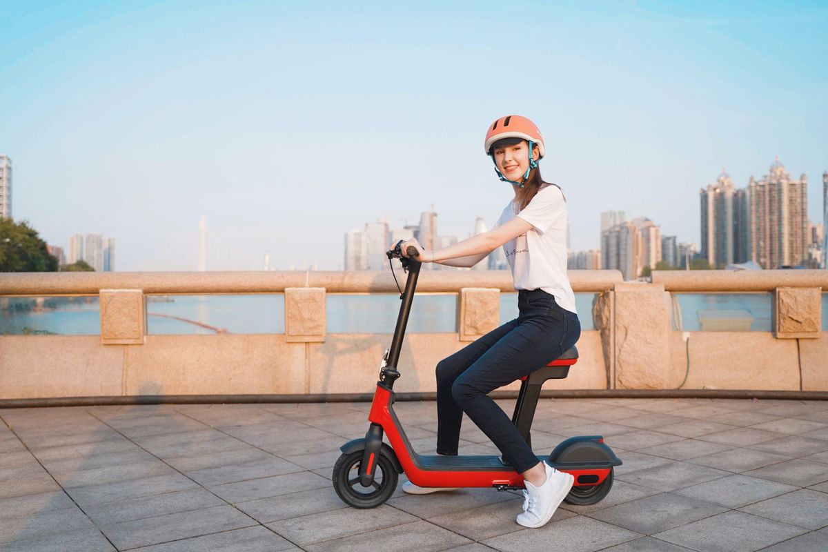 Smiling woman in helmet riding an electric scooter outdoors near a city waterfront