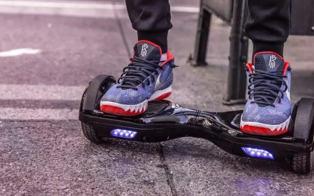 A teenager standing on a black hoverboard with blue LED wheels on a city street