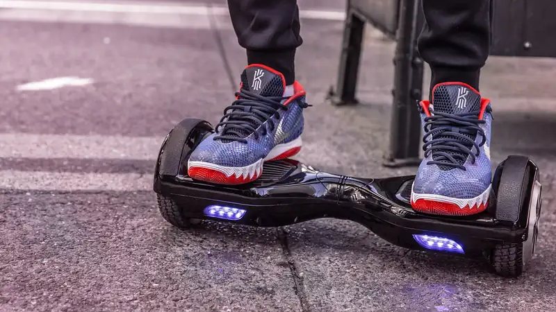 A teenager standing on a black hoverboard with blue LED wheels on a city street