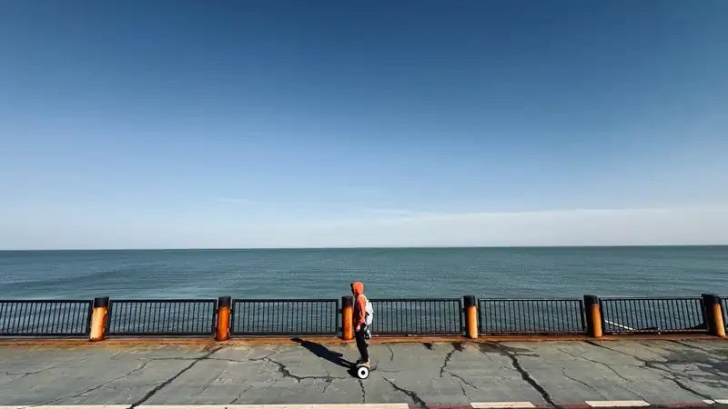 A teenager riding a hoverboard along a seaside promenade