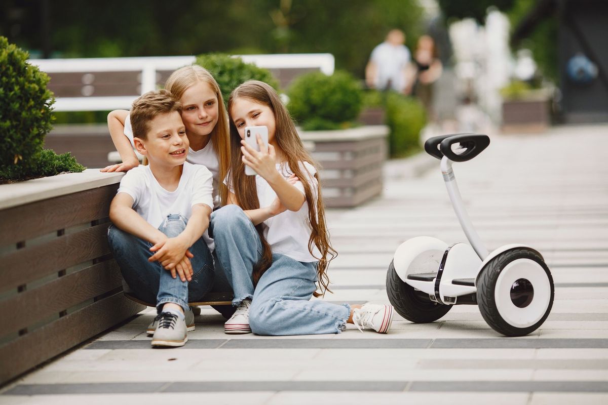Three children taking a selfie outdoors with a self-balancing scooter nearby