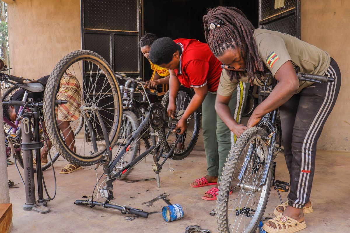 Three women collaboratively repairing bicycles in an indoor workshop