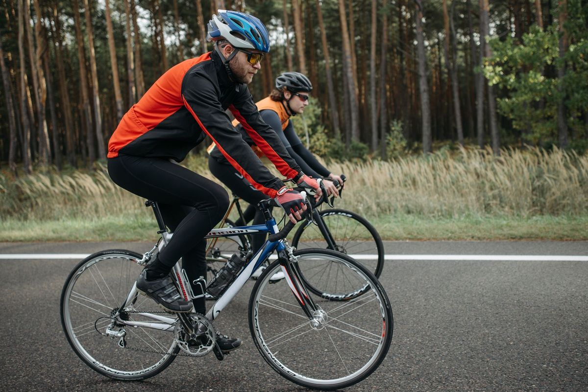 Two adult men cycling on a road surrounded by lush forest, enjoying outdoor exercise